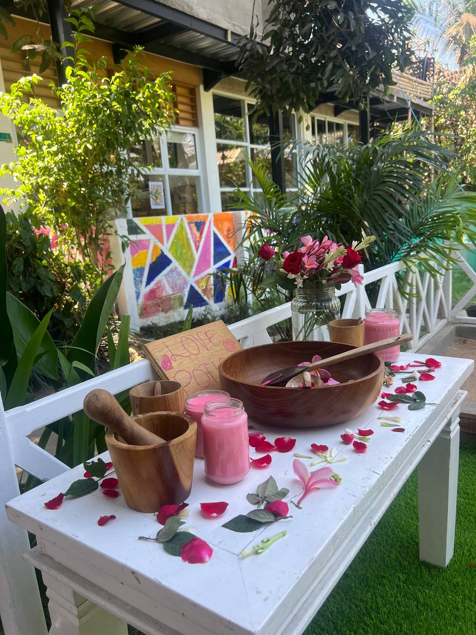 Outdoor atelier table set with a wooden bowl, mortar, rose petals, and a Love Potion sign