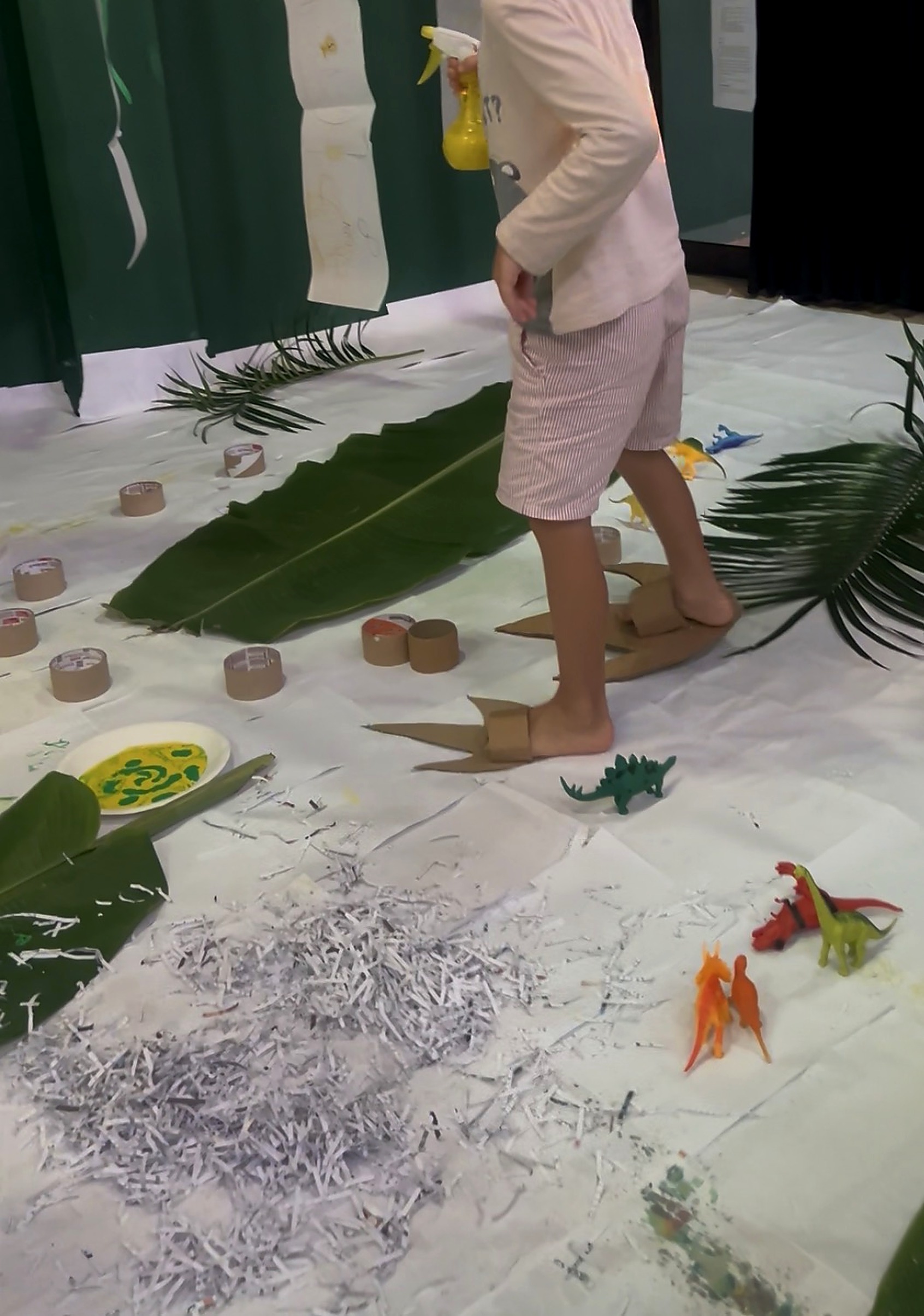 Dinosaur Era - young explorer with cardboard dinosaur feet among palm leaves and figures